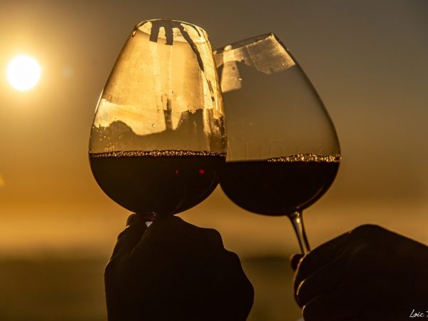 deux mains qui tiennent un verre de vin trinquent au lever du soleil